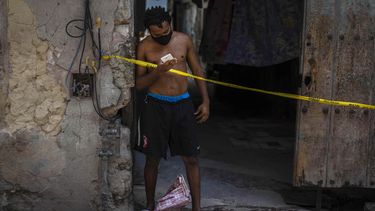 Un hombre que usa una máscara como precaución contra la propagación del nuevo coronavirus mira su teléfono inteligente desde la entrada de su casa en cuarentena en La Habana, Cuba. 