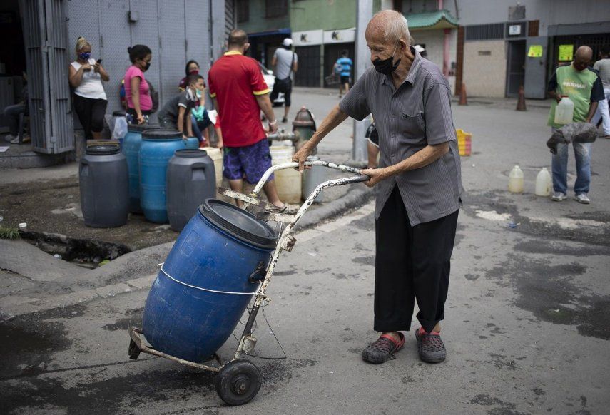 Un hombre, protegido con una mascarilla, empuja un recipiente que llenó de agua en un grifo callejero, en Caracas, Venezuela, el 20 de junio de 2020.&nbsp;