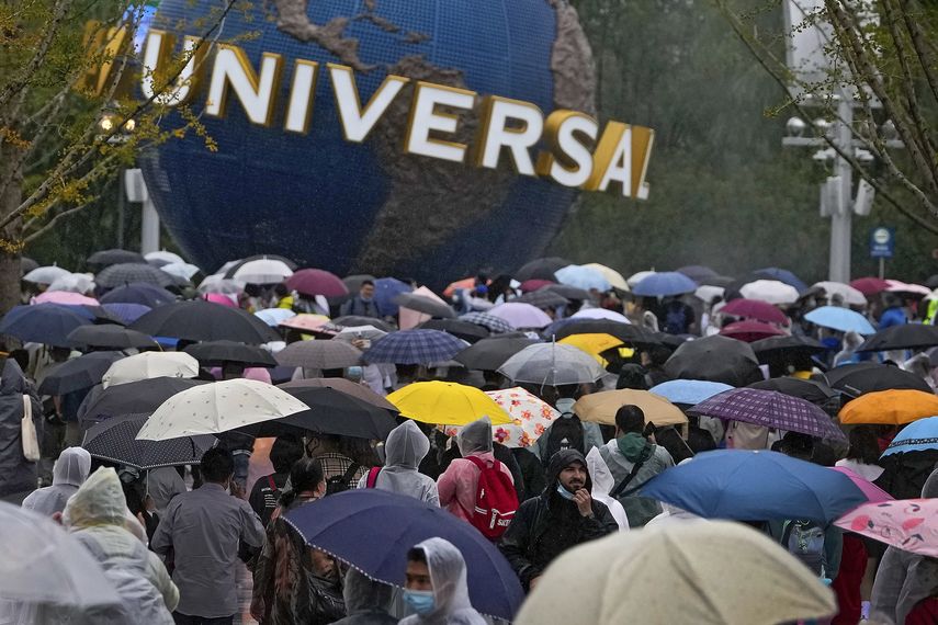 Personas con impermeables y paraguas caminan por una plaza cerca de la entrada de Universal Studios Beijing en Beijing, el 20 de septiembre de 2021. Miles de personas asistieron a la inauguración del parque temático a pesar de la lluvia. AP/Andy Wong