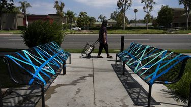 Una mujer camina frente a unas bancas inhabilitadas para implementar las medidas de distanciamiento social afuera de un restaurante en La Habra, California, el jueves 2 de julio de 2020.