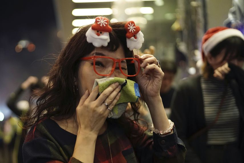 Una mujer con adornos navide&ntilde;os en su cabeza reacciona a gas lacrim&oacute;geno cuando la polic&iacute;a confronta a manifestantes en Nochebuena en Hong Kong, el martes 24 de diciembre de 2019.&nbsp;