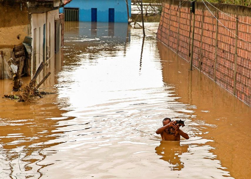 Un hombre carga a su perro en una calle inundada en Itapetinga, estado de Bahia, Brasil, el lunes 27 de diciembre de 2021.