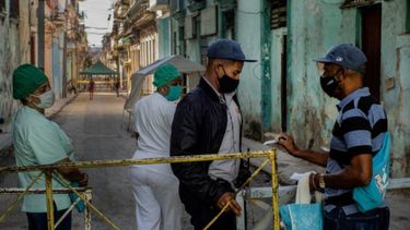 Un residente muestra su identificación a un oficial de policía que está limitando el acceso a un vecindario como una forma de frenar la propagación de la pandemia de COVID-19, mientras enfermeras están detrás en La Habana, Cuba.
