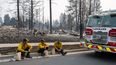 Tres miembros del Departamento de Bomberos de Spokane están sentados en el bordillo frente a viviendas calcinadas en el barrio de Balboa, en Spokane (Washington), el 2 de agosto de 2026