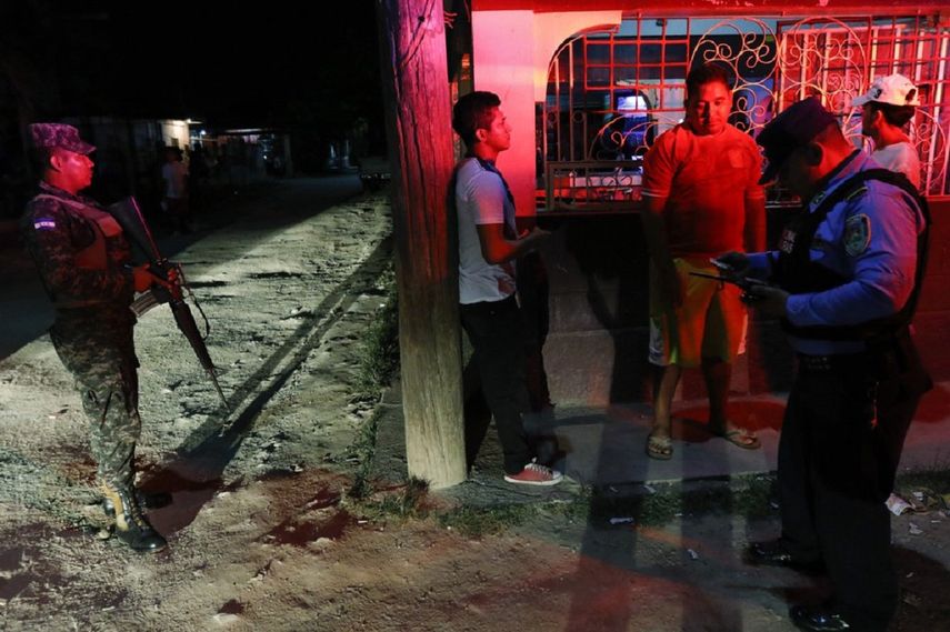 Un soldado protege a un policía que comprueba identificaciones de varios hombres durante una patrulla rutinaria en San Pedro Sula, Honduras, el miércoles 1 de mayo de 2019.&nbsp;