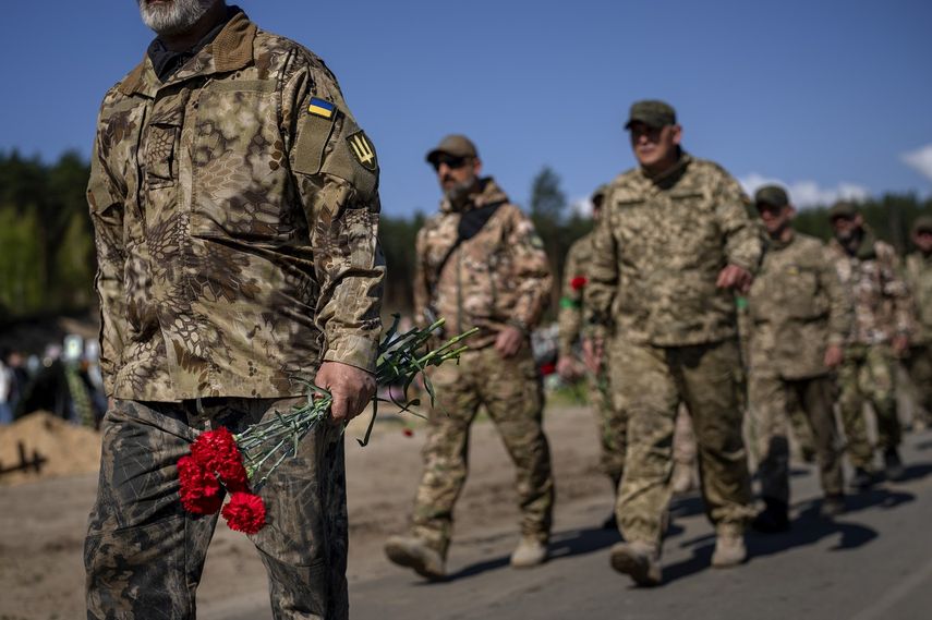 Soldados de la fuerza de defensa territorial de Irpin y del Ejército ucraniano llevan flores para depositar en las tumbas de sus compañeros caídos durante la ocupación rusa, en el cementerio de Irpin, a las afueras de Kiev, el 1 de mayo de 2022.&nbsp;