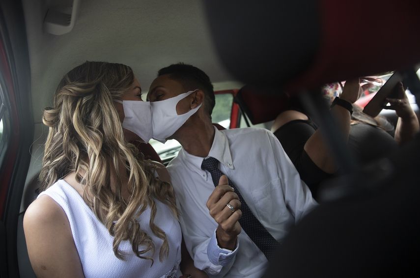 Con mascarillas para evitar la propagaci&oacute;n del coronavirus, Thiago do Nascimento (derecha) y Keilla de Almeida se besan durante su boda, en el drive-thru de un registro en el vecindario de Santa Cruz, R&iacute;o de Janeiro, Brasil, el 28 de mayo de 2020. Las parejas comenzaron a recurrir a esta forma poco convencional de contraer matrimonio en una notar&iacute;a en Santa Cruz desde el inicio de la pandemia en el pa&iacute;s.&nbsp;