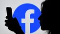 Una joven observa su celular con el logo de Facebook detrás. Una joven observa su celular con el logo de Facebook detrás.