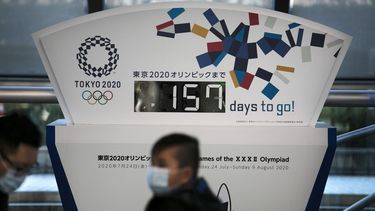 En esta fotograf&iacute;a del martes 18 de febrero de 2020, unas personas que portan mascarillas caminan frente a un reloj de cuenta regresiva para los Juegos Ol&iacute;mpicos en Tokio.&nbsp;