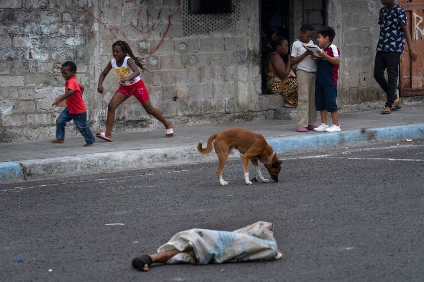Las piernas de un hombre descuartizado sobresalen de una bolsa tirada en una calle donde hay niños jugando y perros, en el vecindario de Colinas de La Florida, en Guayaquil, Ecuador.