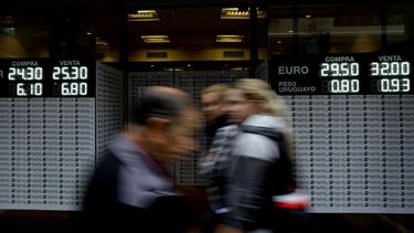 Personas caminando por delante de una casa de cambio de divisa que muestra las tasas del peso argentino frente a otras monedas en Buenos Aires, Argentina, el lunes 14 de mayo de 2018.