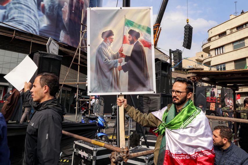 Un hombre sostiene un cartel con la imagen del nuevo líder supremo de Irán, el ayatolá Mojtaba Jamenei (der.), junto a su difunto padre, Alí Jamenei, durante una manifestación en su apoyo en la plaza Enghelab, en el centro de Teherán, el 9 de marzo de 2026.  