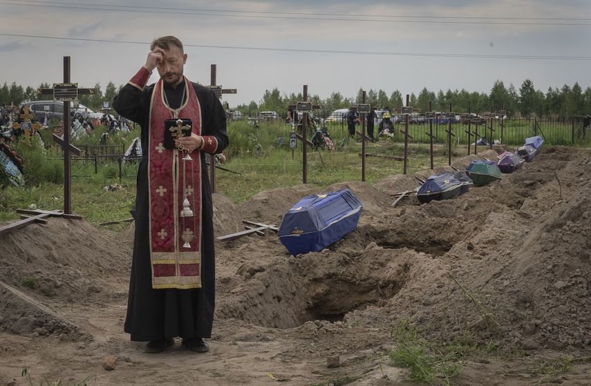 Un sacerdote ora por los restos de civiles no identificados antes de que sean enterrados el jueves 11 de agosto de 2022 en Bucha, en las afueras de Kiev, Ucrania.&nbsp;