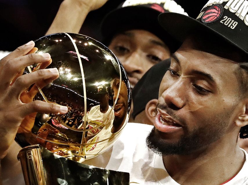 El jugador de los Toronto Raptors Kawhi Leonard (c) sostiene el trofeo del Campeonato de la NBA Larry OBrien luego de vencer a los Golden State Warriors al final del sexto partido de las Finales de la NBA entre Toronto Raptors y Golden State Warriors.