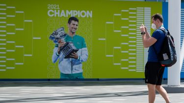 Aficionados sacan una foto frente a un cartel con la imagen del campeón defensor Novak Djokovic previo al Abierto de Australia en Melbourne Park, el martes 11 de enero de 2022