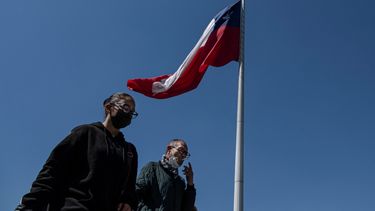 Personas con mascarillas pasan junto a una bandera nacional chilena en una calle peatonal de Santiago, el 21 de septiembre de 2022. Chile anunció el miércoles que levantará las restricciones por la pandemia casi dos años y medio después de imponer las limitaciones.