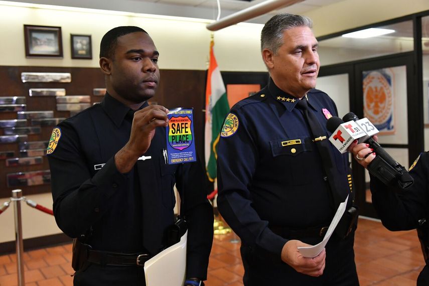 De izq. a derecha: Christopher Moss, vocero de la policía de Miami, quien muestra la calcomanía que identificaría a los negocios de la ciudad como sitios seguros para la comunidad LGBTQ. A su lado, está el jefe de la policia del municipio, Rodolfo Llanes.&nbsp;