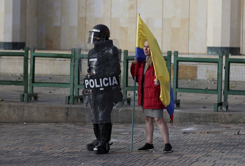En esta imagen, tomada el 21 de septiembre de 2020, una mujer con una bandera colombiana, junto a un agente antimotines durante una protesta en Bogot&aacute;, Colombia. Sindicatos y grupos de estudiantes convocaron manifestaciones contra la brutalidad policial, la inseguridad y la crisis provocada por la pandemia del coronavirus.&nbsp;
