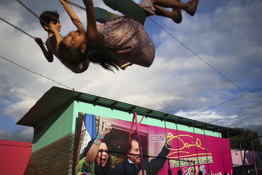 En esta fotografía de archivo del 4 de noviembre de 2016, dos niños se mecen en columpios junto a una propaganda electoral que promueve a Daniel Ortega y a su compañera de fórmula, su esposa Rosario Murillo, en Managua, Nicaragua.