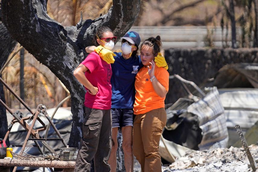 Tres mujeres se abrazan tras rebuscar entre los escombros de una vivienda destrozada por un incendio, el 11 de agosto de 2023, en Lahaina, Hawai. 