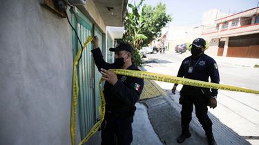 Un policía marca un perímetro de seguridad alrededor de una casa donde realizan una investigación en México. 