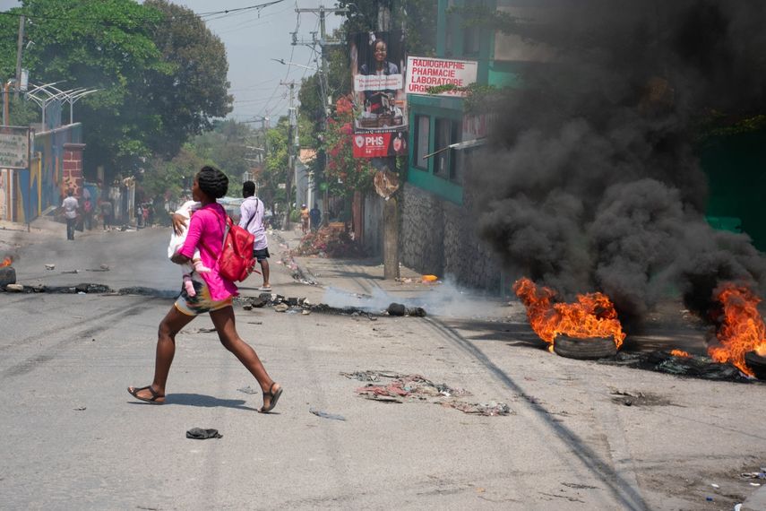 Una mujer con un niño en brazos corre por una calle de Puerto Príncipe, en medio de disturbios provocados por las pandillas.