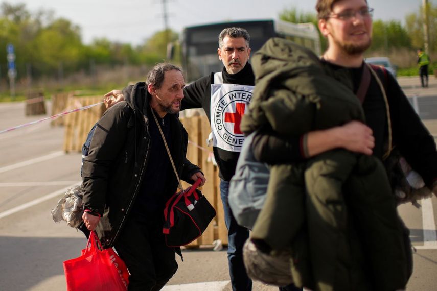 Personal de la Cruz Roja da instrucciones a Serhii Tsybulchenko (izq) y su yerno Ihor Trotsak a su llegada a Zaporiyia (Ucrania) tras la evacuación de unas 100 personas de una planta siderúrgica de Mariúpol (Ucrania). Foto del 3 de mayo del 2022.