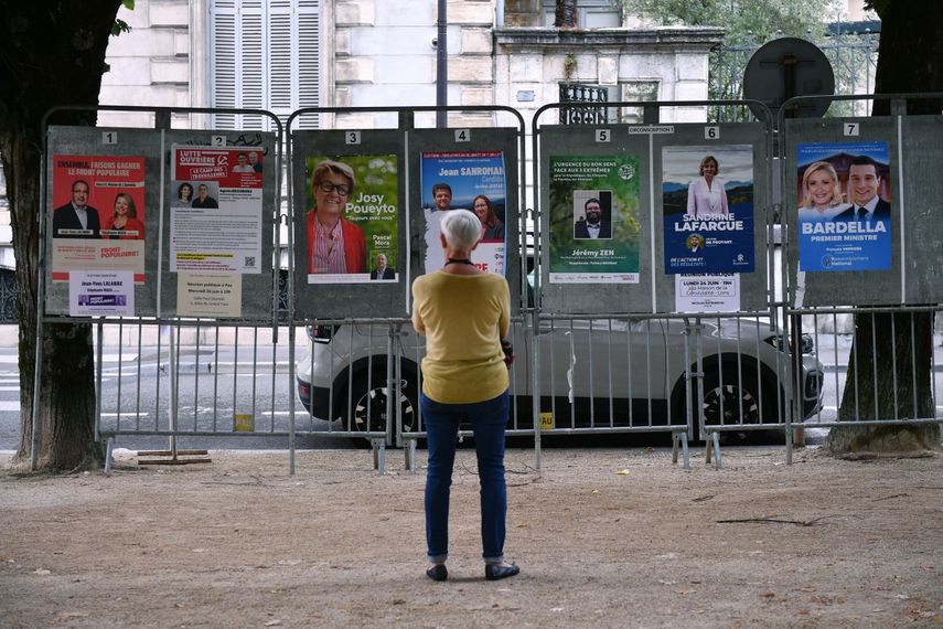 Una mujer mira carteles electorales junto a un colegio electoral durante la primera ronda de las elecciones parlamentarias en Pau, suroeste de Francia, el 30 de junio de 2024.