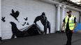 Un guardia de seguridad pasa junto a una obra de arte del artista callejero Banksy, la novena que se publica en nueve días, que representa a un gorila liberando animales, en el frente de una persiana afuera del zoológico de Londres, el 13 de agosto de 2024. &nbsp;