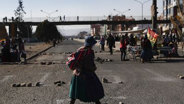 Una mujer que usa una mascarilla para prevenir el nuevo coronavirus camina por una calle bloqueada por manifestantes que protestan contra la postergaci&oacute;n de las elecciones presidenciales en El Alto, Bolivia, el mi&eacute;rcoles 5 de agosto de 2020.