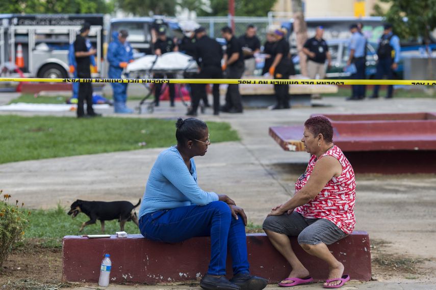 Un par de vecinos habla mientras la polic&iacute;a, al fondo, retira cad&aacute;veres de v&iacute;ctimas de una masacre armada en San Juan, Puerto Rico, el martes 15 de octubre del 2019.&nbsp;