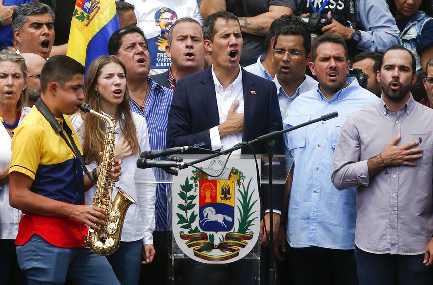 El presidente encargado de Venezuela, Juan Guaidó, canta el himno nacional mientras un músico toca el saxofón en un acto de masas en Caracas.