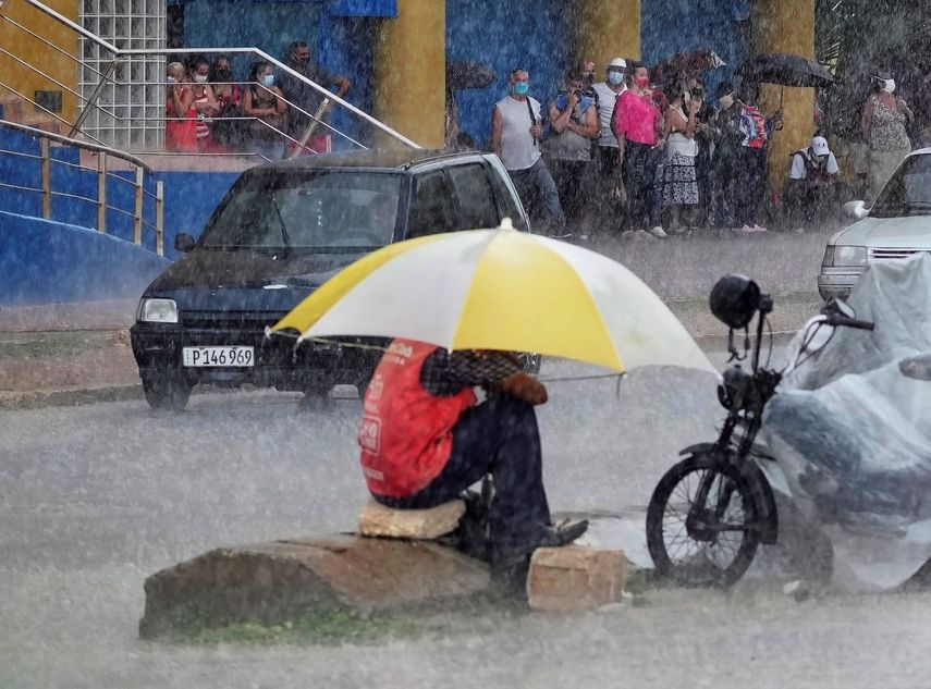 Un valet usa un paraguas para protegerse de un aguacero mientras la gente hace cola en la entrada de una tienda estatal de dólares en La Habana, Cuba.