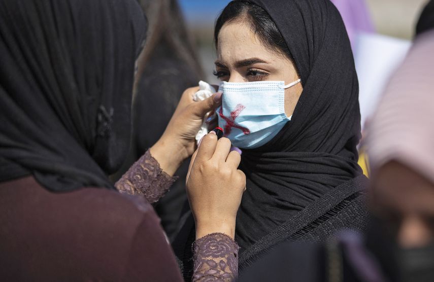 En esta foto de archivo tomada el 8 de marzo de 2021, una manifestante usa lápiz labial para tachar la máscara de otra manifestante mientras asiste a una manifestación por el Día Internacional de la Mujer en la ciudad de Basora, en el sur de Irak.&nbsp;