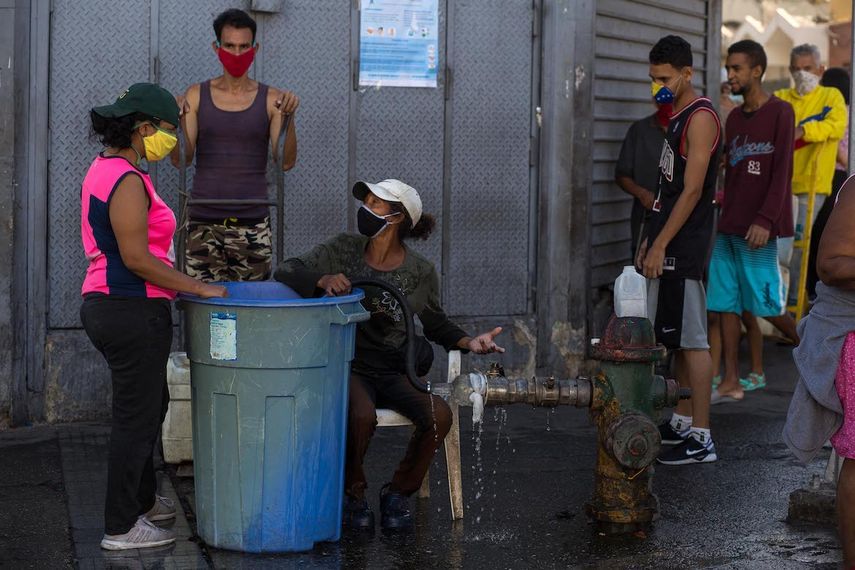 Las personas usan mascarillas como medida preventiva contra la pandemia mundial de coronavirus COVID-19 mientras esperan para recoger agua de una tuber&iacute;a de la calle en Caracas, el 27 de marzo de 2020.&nbsp; &nbsp; &nbsp;