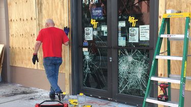Un hombre trata de proteger su negocio en Miami tras destrozos causados por protesta.