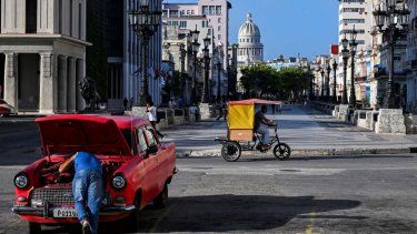 Un hombre repara su antiguo carro en medio de la calle, mientras un hombre en su bicitaxi busca clientes a quienes llevar en una de las calles de La Habana, Cuba.