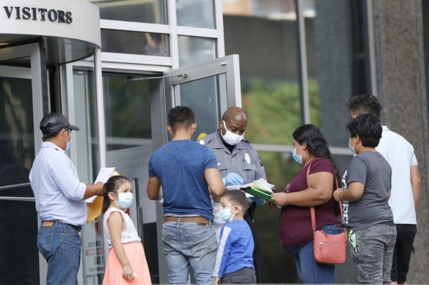 Un agente de seguridad, al centro, revisa los papeles de unas personas frente a un edificio federal con el fin de darles una forma para que regresen otro día a realizar sus trámites de inmigración, en Baltimore.&nbsp;