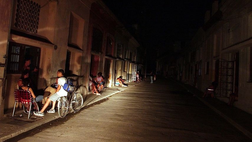 Varias personas conversan iluminadas por la luz de un automóvil en una calle del populoso barrio El Cerro, en La Habana, Cuba.