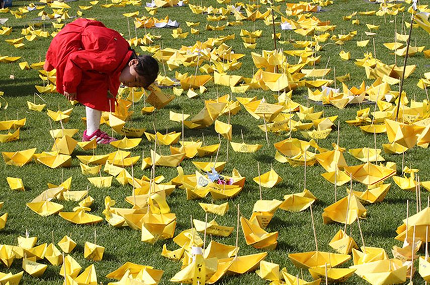 Una niña lee los mensajes colocados en barcos de papel para las víctimas del naufragio del transbordador Sewol en una ceremonia fúnebre el 5 de mayo de 2014 en Seúl, Corea del Sur. (AP)