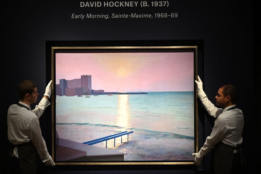 En esta foto de archivo tomada el 6 de octubre de 2022, los asistentes de la galería sostienen el cuadro titulado Early morning, Sainte-Maxime, 1968-69 del pintor británico David Hockney durante una sesión fotográfica para 20th/21st Century: London Evening Sale at Christies en Londres.