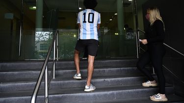 Un joven con la camiseta del dorsal 10, que usó Maradona, posa frente a la clínica en la que está internado el astro del balompié