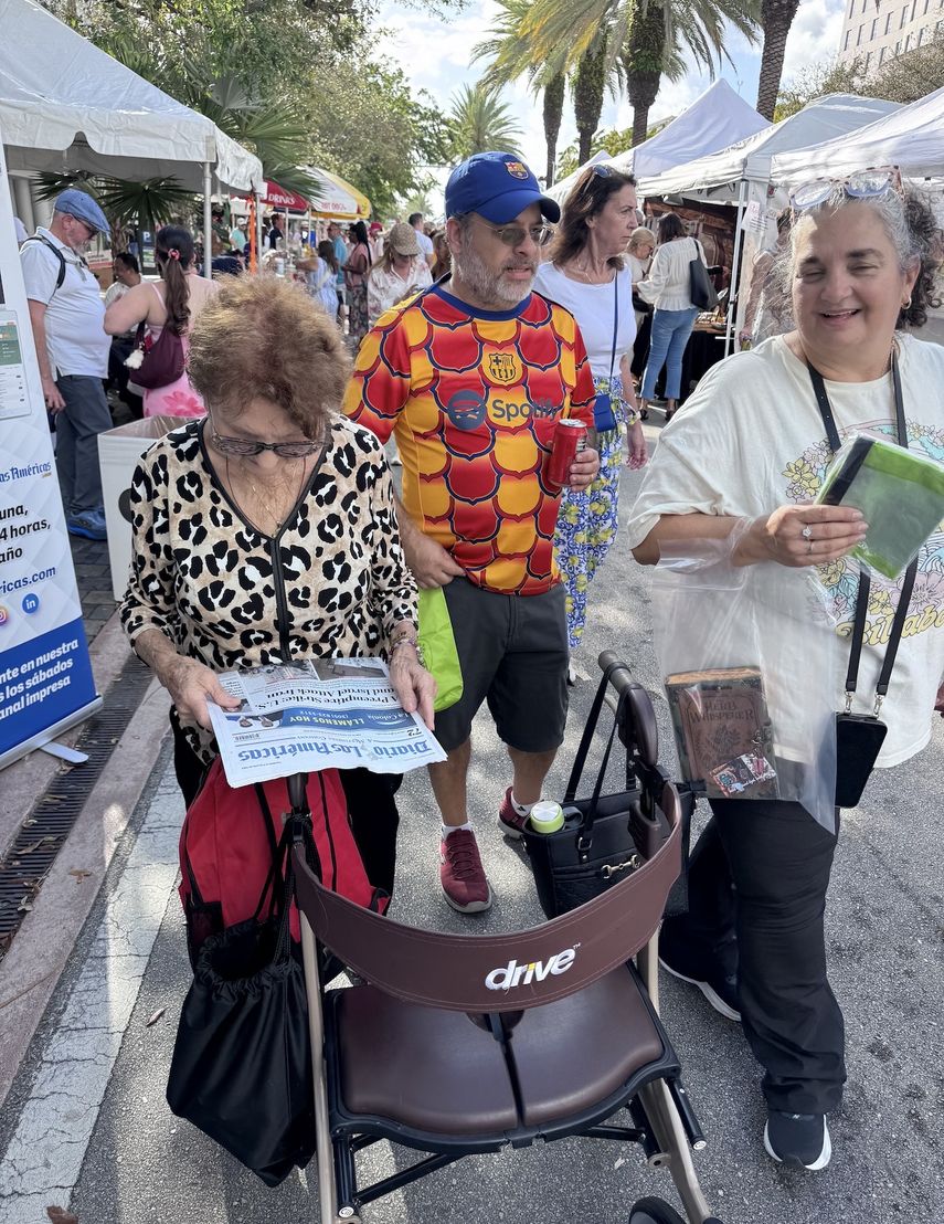 Asistentes caminan entre los puestos mientras hojean la edición impresa del periódico.