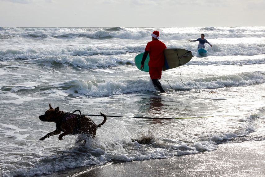 Un surfista vestido de Papá Noel lleva una tabla de surf durante el 15º evento anual 