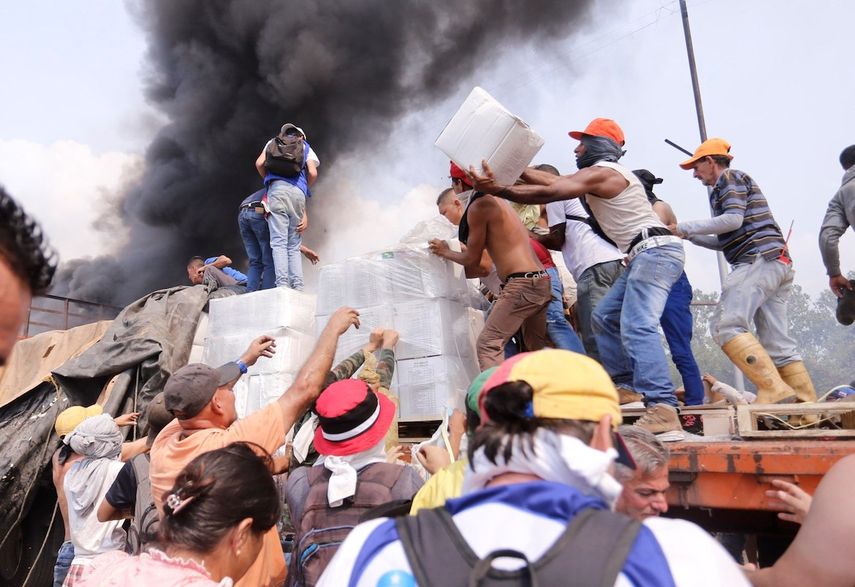 Voluntarios rescatan las cajas con la ayuda humanitaria que fue quemada por grupos irregulares a disposición del régimen de Nicolás Maduro.&nbsp;
