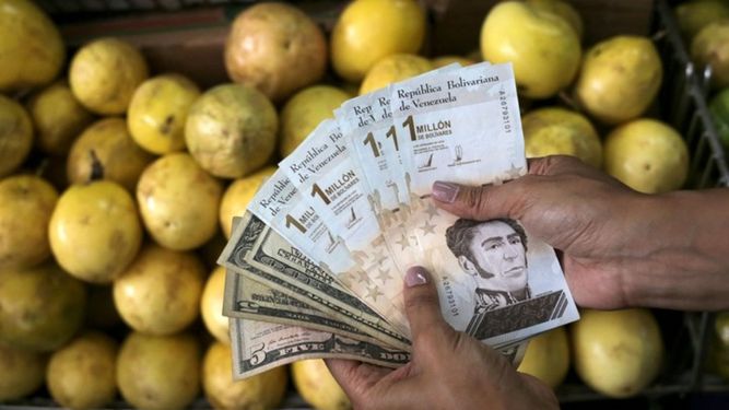 Un cliente muestra billetes de bolívares y de dólar, en un mercado de Caracas