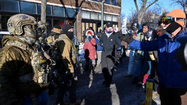 Agentes federales observan mientras los manifestantes se reúnen cerca del lugar donde las autoridades estatales y locales dicen que un hombre fue baleado por agentes federales más temprano esa mañana en Minneapolis, Minnesota, el 24 de enero de 2026.