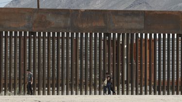 Fotografía del 17 de julio de 2019 de tres migrantes que caminan junto a la valla fronteriza en El Paso, Texas, tras cruzar el río Bravo desde territorio mexicano.