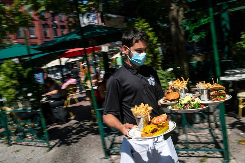Un camarero con una mascarilla para protegerse del coronavirus entrega comida en la sección al aire libre de un restaurante, el viernes 4 de septiembre del 2020, en Hoboken, Nueva Jersey. 