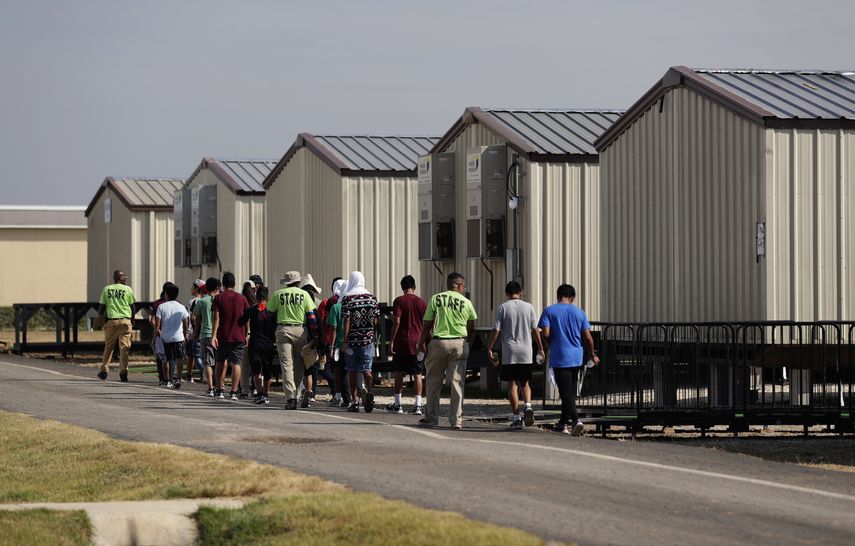 Personal del nuevo centro de detención de migrantes menores de edad de Carrizo Springs, Texas, acompaña a algunos muchachos a las estructuras rodantes que funcionan como habitaciones.